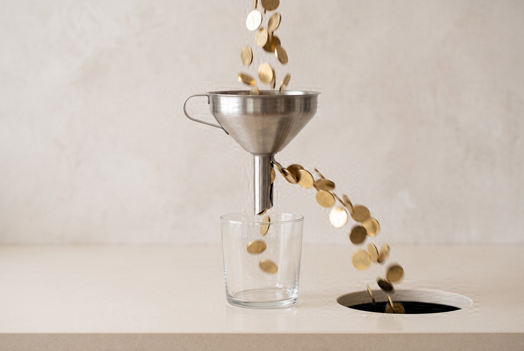 A steel funnel with a split stem. Most of the brass coins poured into it escape sideways and fall down a hole in the counter. The glass below has caught almost none.